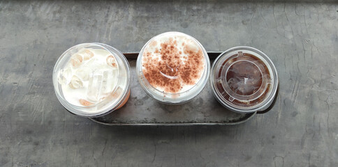 Three kinds of drinks in plastic glasses are placed in a steel tray placed on a cement table from top view.