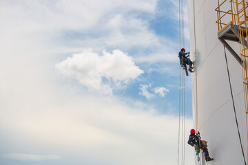 Male workers control rope down height tank rope access inspection of thickness shell plate tank.