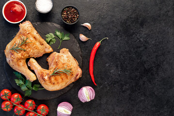 two grilled chicken legs with spices and herbs on a stone background with copy space for your text