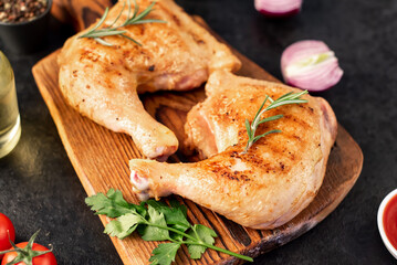 two grilled chicken legs with spices and herbs on a stone background