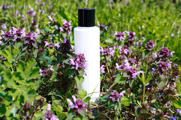 Mock Up bottle of shampoo standing in a meadow with flowering Lamium purpureum, dead-nettle, purple dead-nettle, or purple archangel. White unbranded dispenser bottle