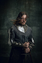 Half-length portrait of brutal seriuos man in image of medieval warrior or knight with dirty...