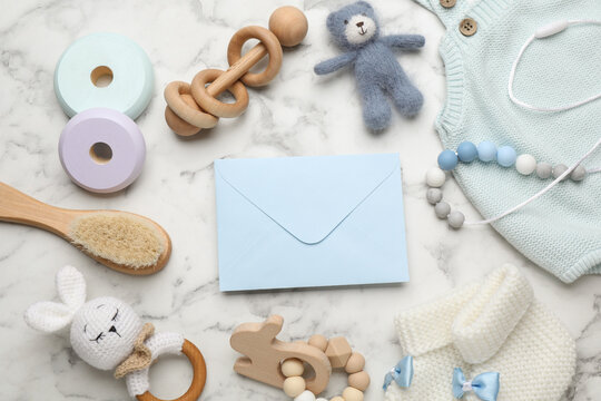 Baby shower party. Envelope surrounded by stuff for child on white marble background, flat lay