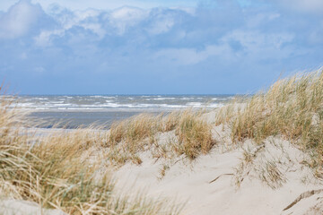 Beach on the North Sea. Small dune with grass and with the North Sea in the background. At the sea in a German travel destination. Promenade in the Netherlands. Vacation in spring	