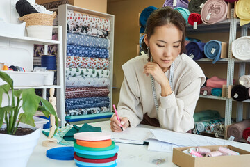Young Asian seamstress drawing clothes sketch in workshop