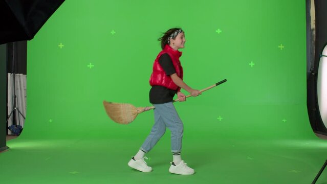 Cute teen girl shows witch flying on broom over green screen. Female kid having fun. Halloween concept. Chroma Key. 4k uhd video footage