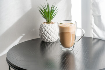Glass of coffee with milk on a table on a white background. Cup of hot latte coffee on the table nearly window.