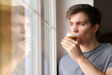 Pensive Caucasian Man with Brunette Hair Drinks Coffee while Looking out of the Window. Attractive Young Adult   with Window Reflection.