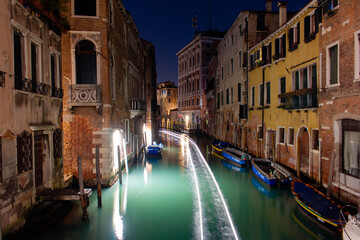 Fototapeta na wymiar Canal in Venice with the lights of a passing boat. Long exposure at night.
