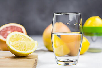 Citrus water in glass on light table against dark gray background. Sliced lemon on wooden board. Selective focus.