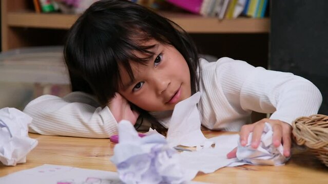 Upset little girl making a colorful drawing at home and crumpled the paper on desk. Girls who are bored with online learning and homework during the coronavirus pandemic.