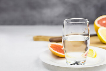 Citrus water in glass on white plate on light table against dark gray background. Sliced lemon and grapefruit on wooden board. Selective focus. Copy space.