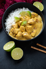 Bowl of yellow curry with chicken meat and white rice, vertical shot on a black stone surface, middle close-up