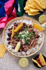 Serving pan with chili con carne, white rice and nachos chips, middle closeup, vertical shot on a beige marble background