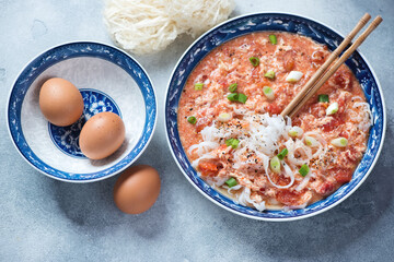 Plate of chinese tomato egg-drop noodle soup on a light-blue stone background, horizontal shot