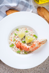 Closeup of crab risotto served in a white plate with a boiled crab claw, vertical shot, elevated view
