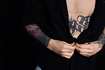 Young man with tattoos wearing black shirt on dark background, closeup