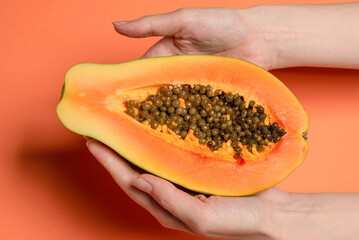 Papaya fruit on a orange background in woman hands. Tropical fruit.