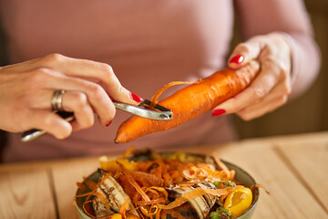 Women scraps peels carrots vegetable peeling, throws in compost bucket, organic composting