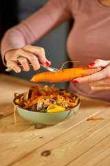 Women scraps peels carrots vegetable peeling, throws in compost bucket, organic composting