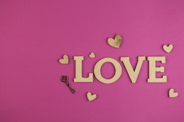 The word Love with small hearts against a pink paper background closeup