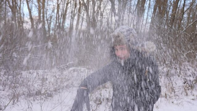 Cute happy smiling european teenage kid playing cheerfully snowball outside in snowy scenic winter forest. Boy catches and brakes ball with his hands