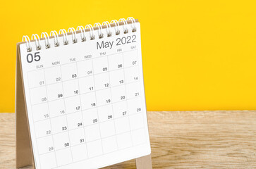 May 2022 desk calendar on wooden table with yellow background.