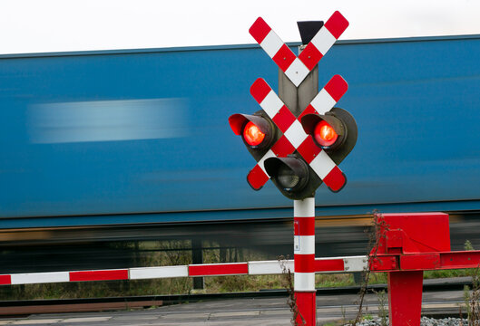Blue freight train wagon passes at crossing with red signal and closed barriers. 