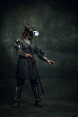 Portrait of man, medieval warrior, knight with dirty wounded face in VR headset isolated over dark...