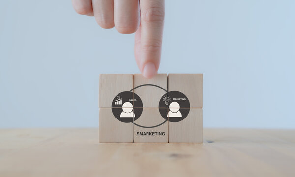 Smarketing concept. Integrated sales and marketing functions to have a common goal and approach. Hands puts the wooden cubes with SMARKETING icons isolated on white background and coppy space.