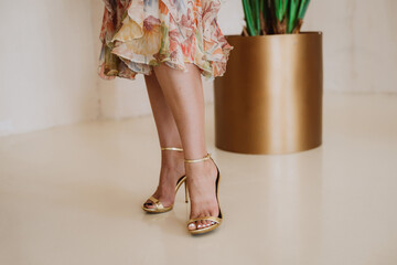Slender female legs in a summer dress with a floral print and open summer golden shoes. Soft...