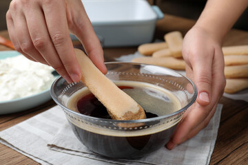 Woman making tiramisu cake at wooden table, closeup