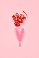 Pink menstrual cup on pink background. Decorated with red ribbon.