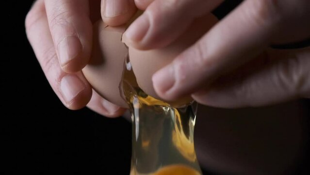 female hands cracking an egg falling down in slow motion close up Black background