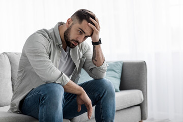 Man sit alone feeling sad worry regret or fear, depressed and desperate in sofa at home