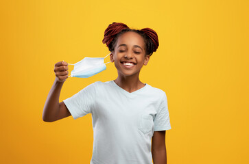 Smiling black girl removing protective face mask