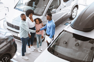 Millennial black family shaking hands with salesman, making deal, buying or renting new vehicle at car dealership