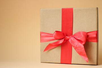 Close up Gift box with red silk bow against beige background.