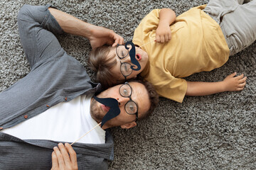 Movember concept. Funny surprised father and and little son wearing eyeglasses holding moustache...