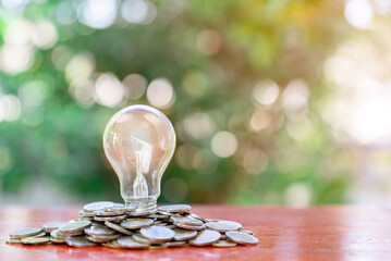 Light bulb sit on stacks of coins on out of focus background.