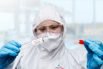 Medical healthcare NHS technician holding,COVID-19 swab collection kit,wearing white PPE protective...