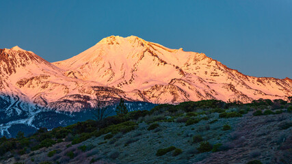 Naklejka premium Snow covered mountain during sunset with a reddish glow and a blue sky.
