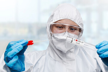Medical healthcare NHS technician holding,COVID-19 swab collection kit,wearing white PPE protective...