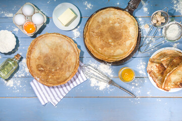 Russian Ukrainian European holiday Maslenitsa. Traditional thin crepes pancakes, on wooden blue table with ingredients for cooking - flour, eggs, butter, top view copy space