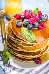 Plate of delicious traditional american pancakes with fresh berries and syrup on kitchen table on light background