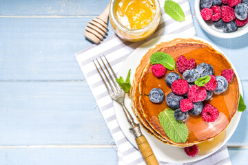 Plate of delicious traditional american pancakes with fresh berries and syrup on kitchen table on light background