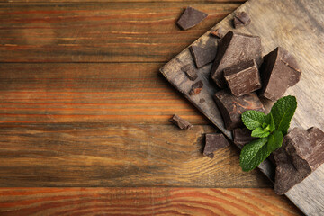 Tasty dark chocolate pieces with mint on wooden table, flat lay. Space for text