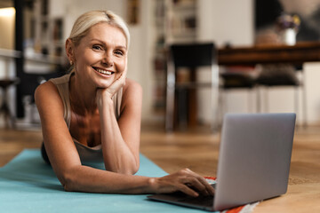 Blonde mature woman smiling and using laptop during yoga practice