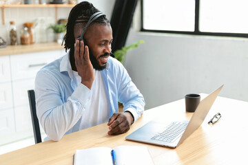 Joyful young adult African american man wears headset working or studying online using laptop computer while sitting at home, online business meeting, video call. smiling