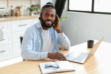Portrait of an African American help desk employee in a headset, working remotely at home using laptop computer, looking at the camera and smiling friendly